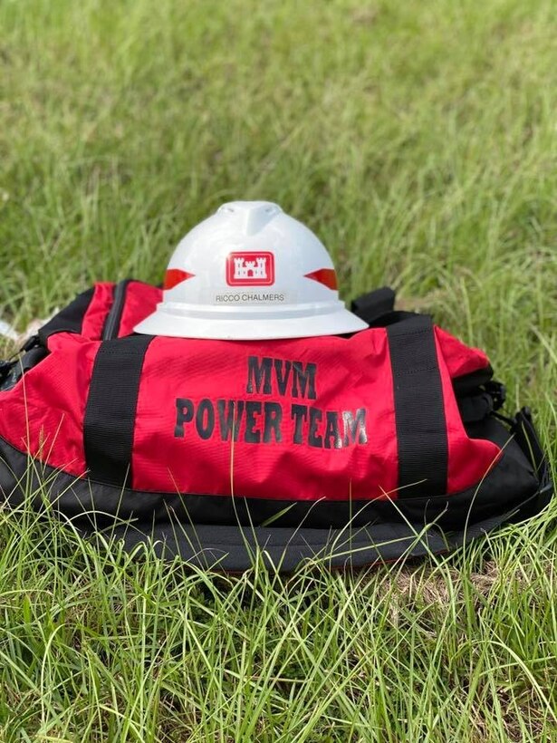 A red duffle bag sits in grassy field with a red and white U.S. Army Corps of Engineers hat on top of it.