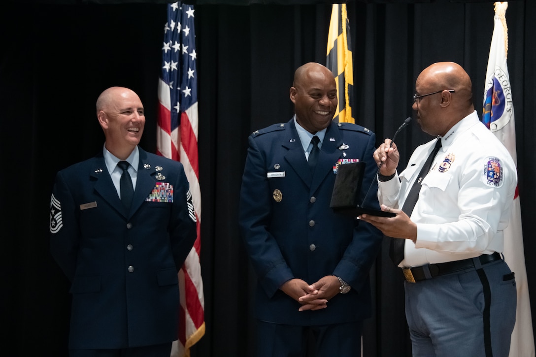Malik Aziz, Prince George's County chief of police, right, presents a gift to U.S. Air Force Col. Todd E. Randolph, 316th Wing and installation commander at Joint Base Andrews, Md., and Chief Master Sgt. Jackson A. Helzer, Command Chief at JB Andrews, during a ceremony at PGPD Headquarter in Upper Marlboro, Md., May 25, 2023. PGPD held the ceremony in honor of Military Appreciation Month and the frequent work that the department does with the base's Security Forces Airmen. (U.S. Air Force photo by Senior Airman Daekwon Stith)