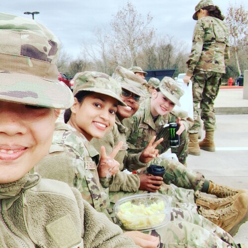 Group of people in military uniform sitting down looking at camera (posing for selfie)