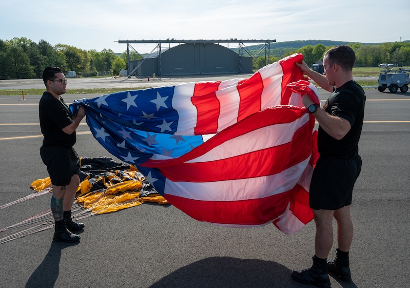 U.S. Army Staff Sgt. Nickolas Orozco and Specialist Brandon Hexum, U.S. Army Golden Knight parachute team demonstrators, prepare the American flag prior to a flight and demonstration during the 2023 Westfield International Air show May 13, 2023, at Barnes Air National Guard Base, Massachusetts. Air shows are a public event held on base to provide an opportunity for people to see U.S. military air capabilities in action and meet the service members who fly and maintain the equipment. (Massachusetts Air National Guard Photo by Tech. Sgt. Kevin R. Nunes)
