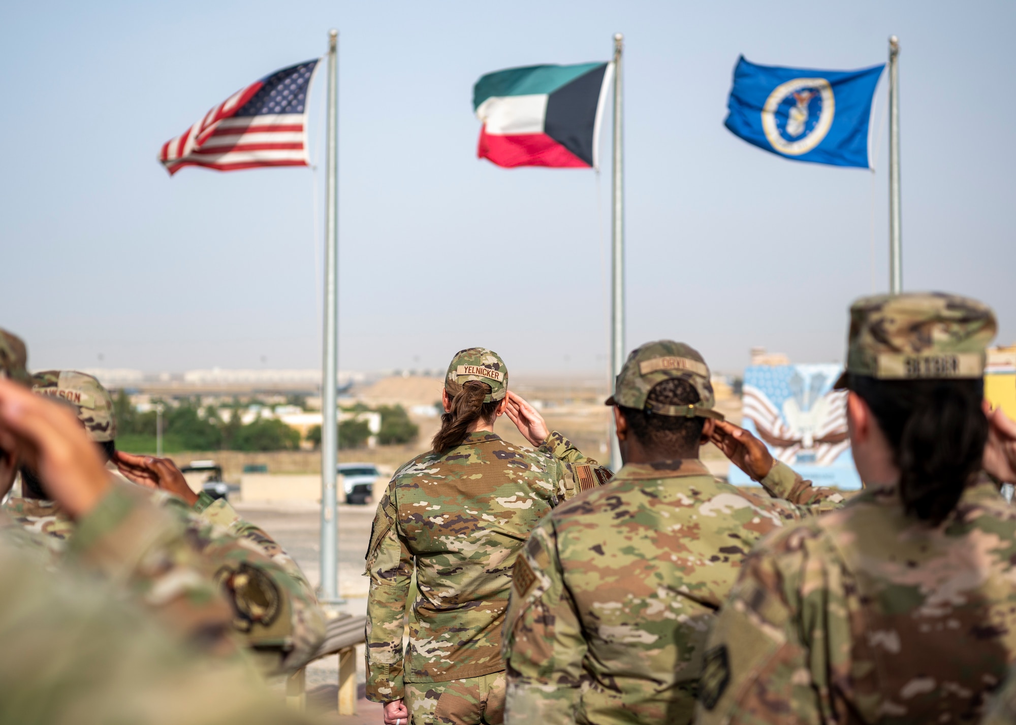 Service members salute U.S. flag, Kuwaiti flag and Air Force flag, during Memorial Day ceremony.