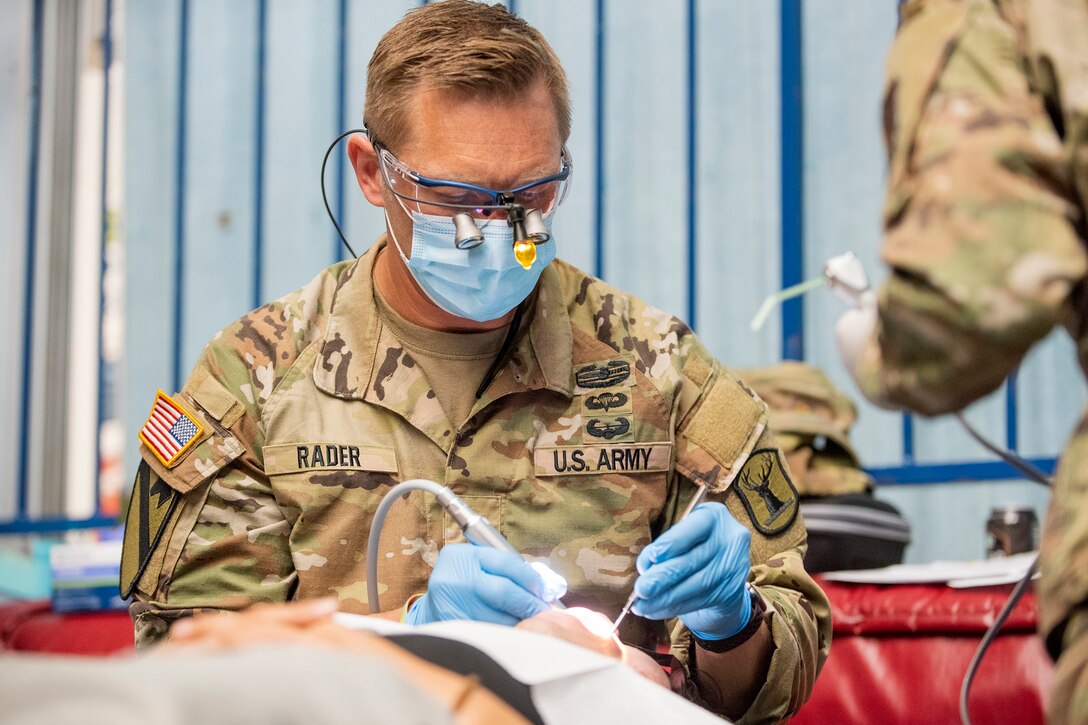 A soldier performs dental work on a patient.