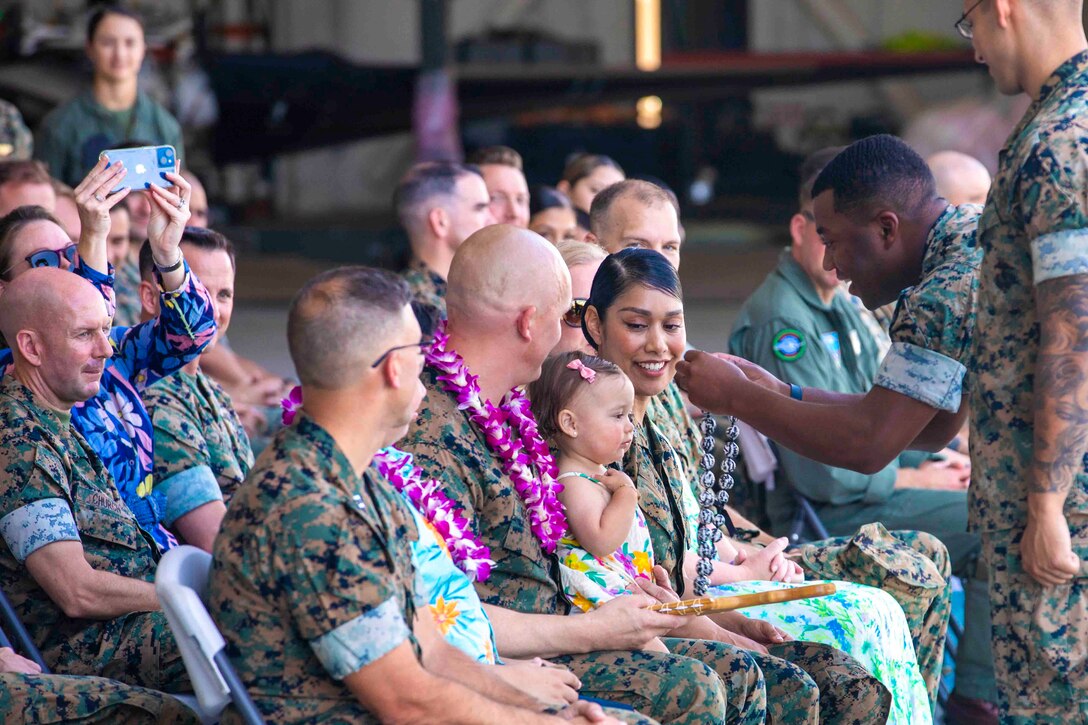 A Marine places a lei on a child sitting in a crowd next to other Marines.