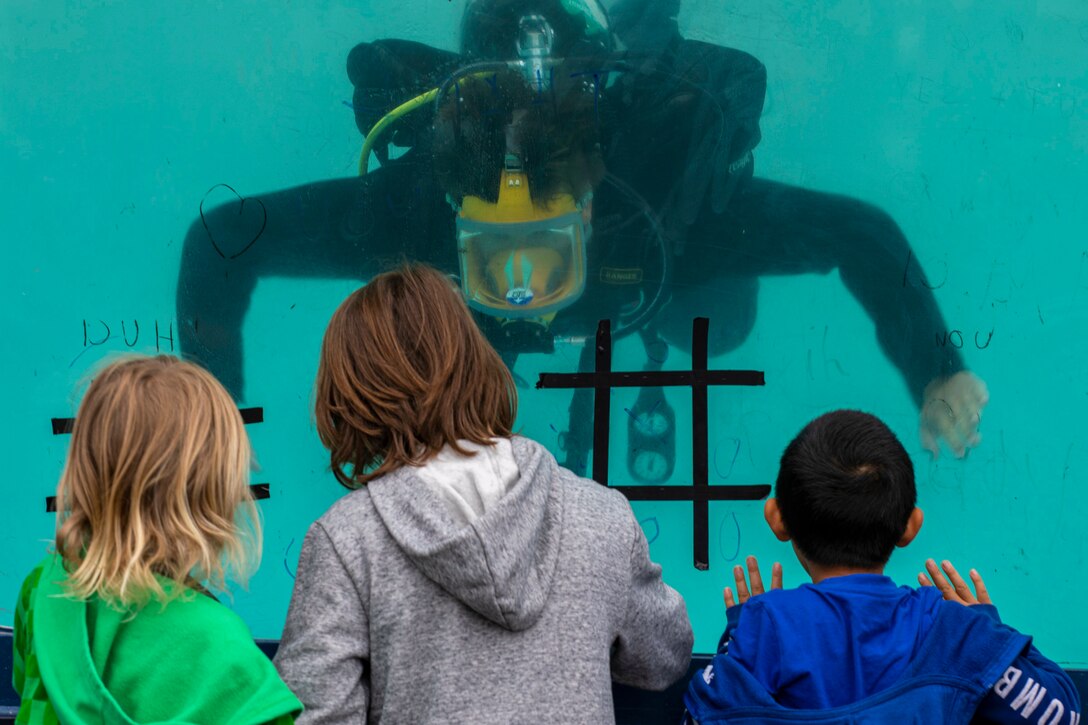 Children watch as a diver floats underwater in a dive tank.