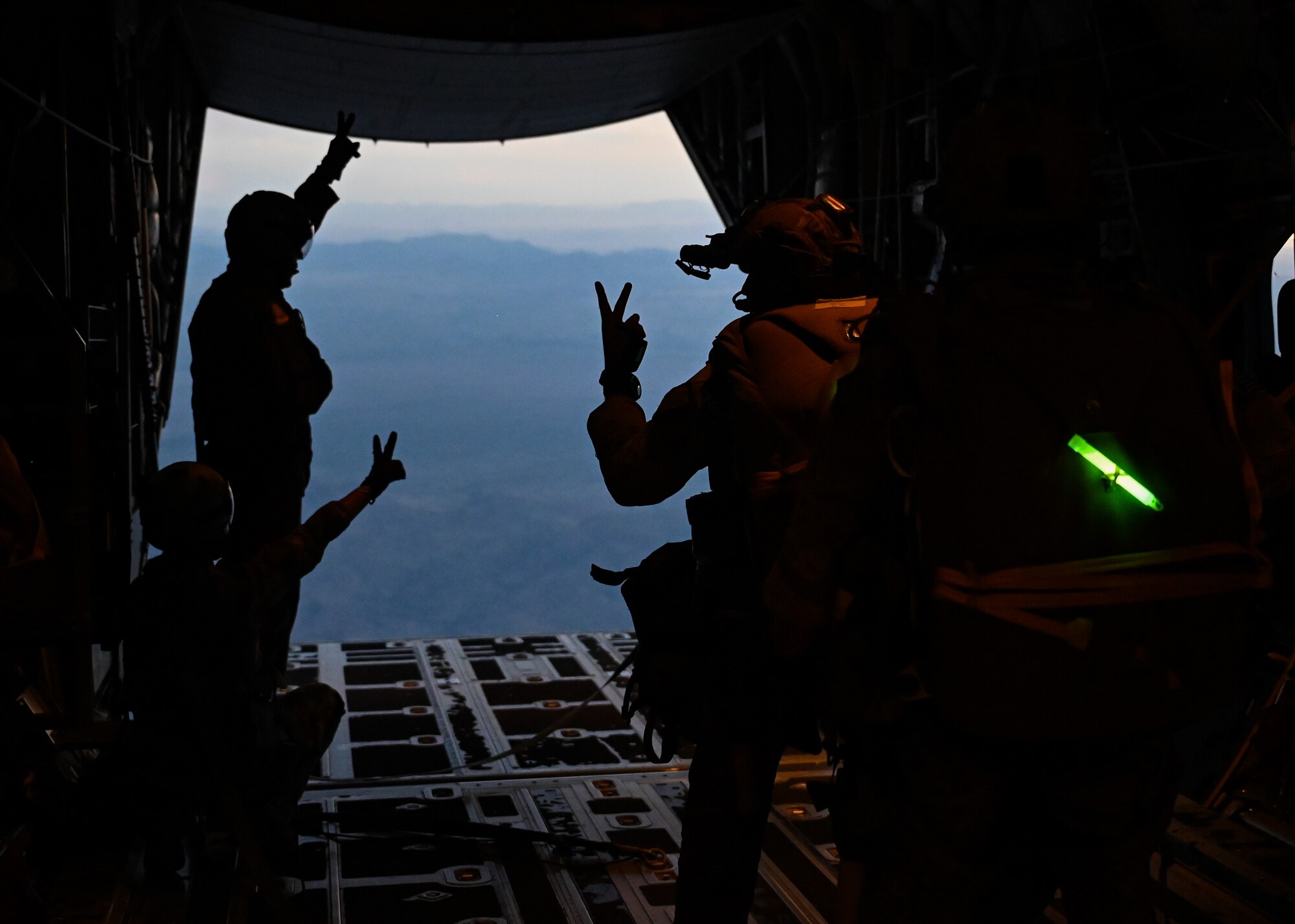 Men in military uniforms and gear prepare to parachute out of an airplane.