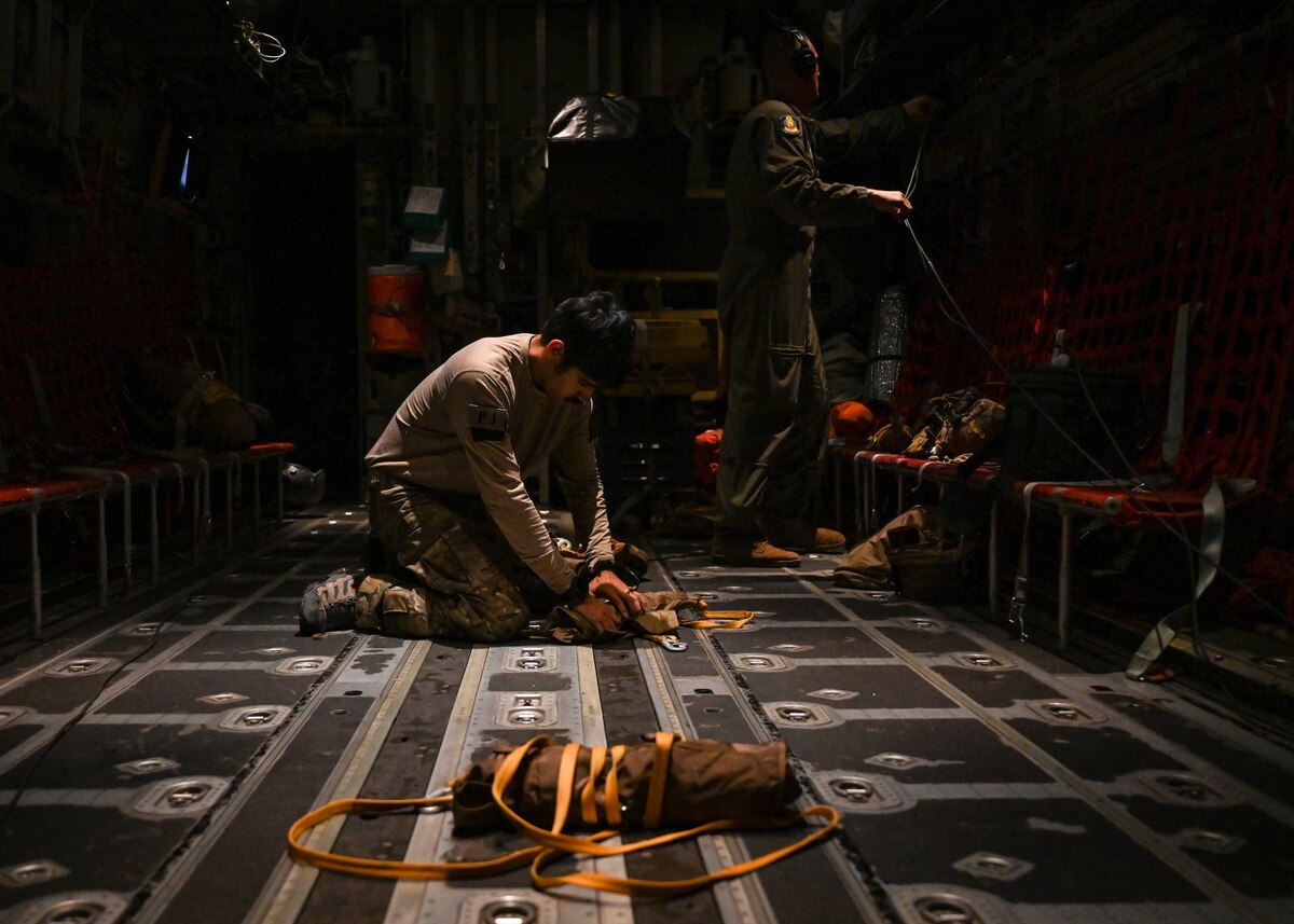 A man in a military uniform packs gear in an aircraft.