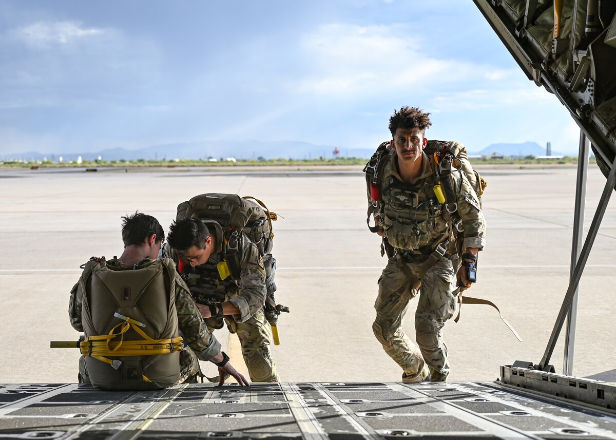 Men in military uniforms put on necessary gear for parachuting out of an airplane.