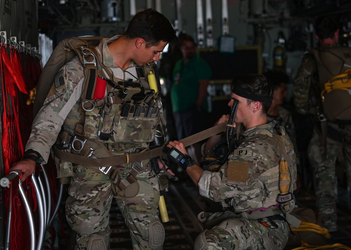 Men in military uniforms prepare their gear to parachute out of an airplane.