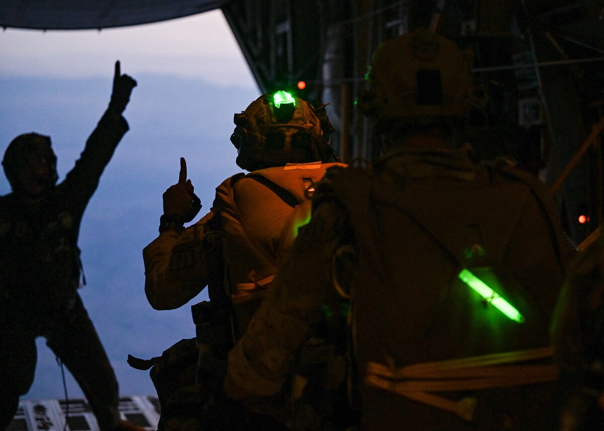 Men in military uniforms prepare to parachute out of an airplane.