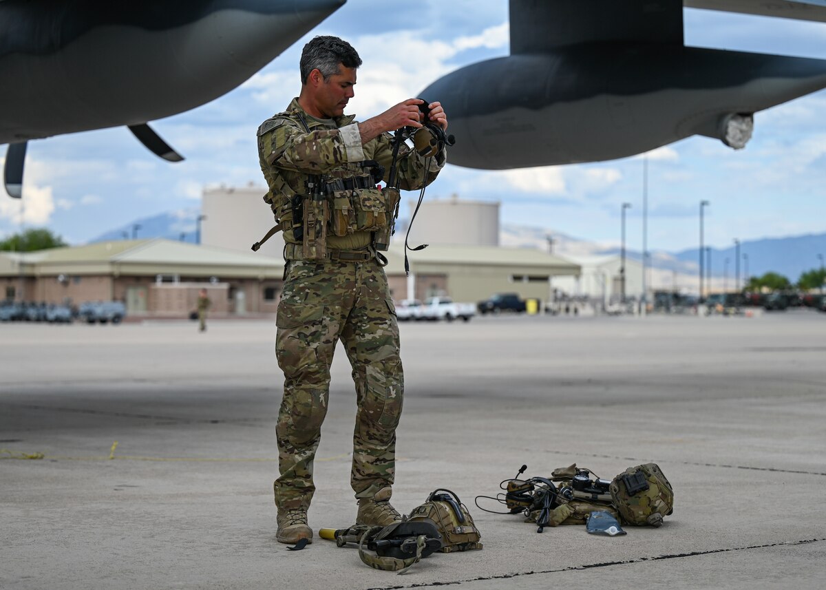 A man in a miliary uniform puts on a helmet needed for parachuting out of an airplane.