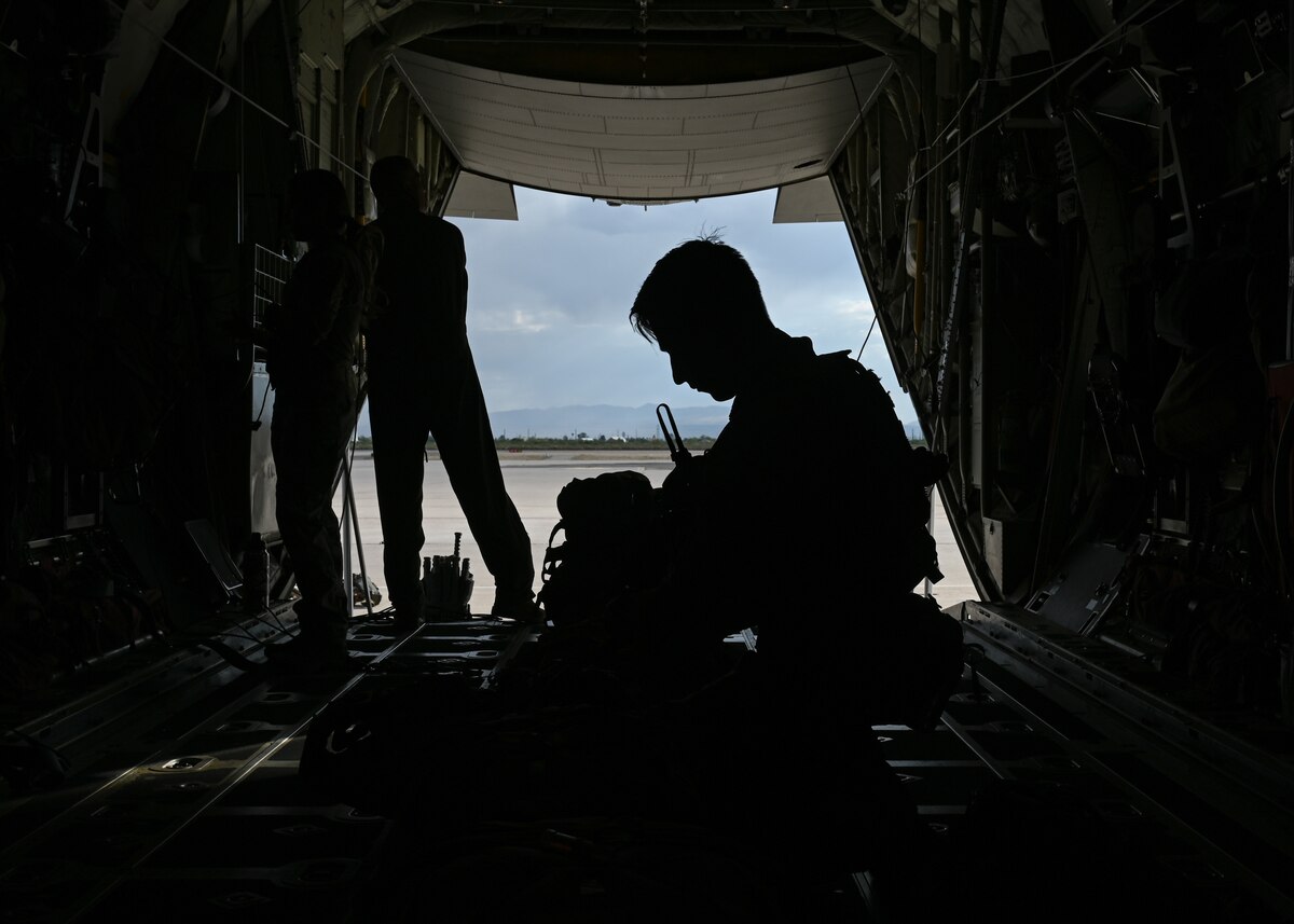 A man in a military uniform checks his bag for necessary gear to parachute from an airplane.