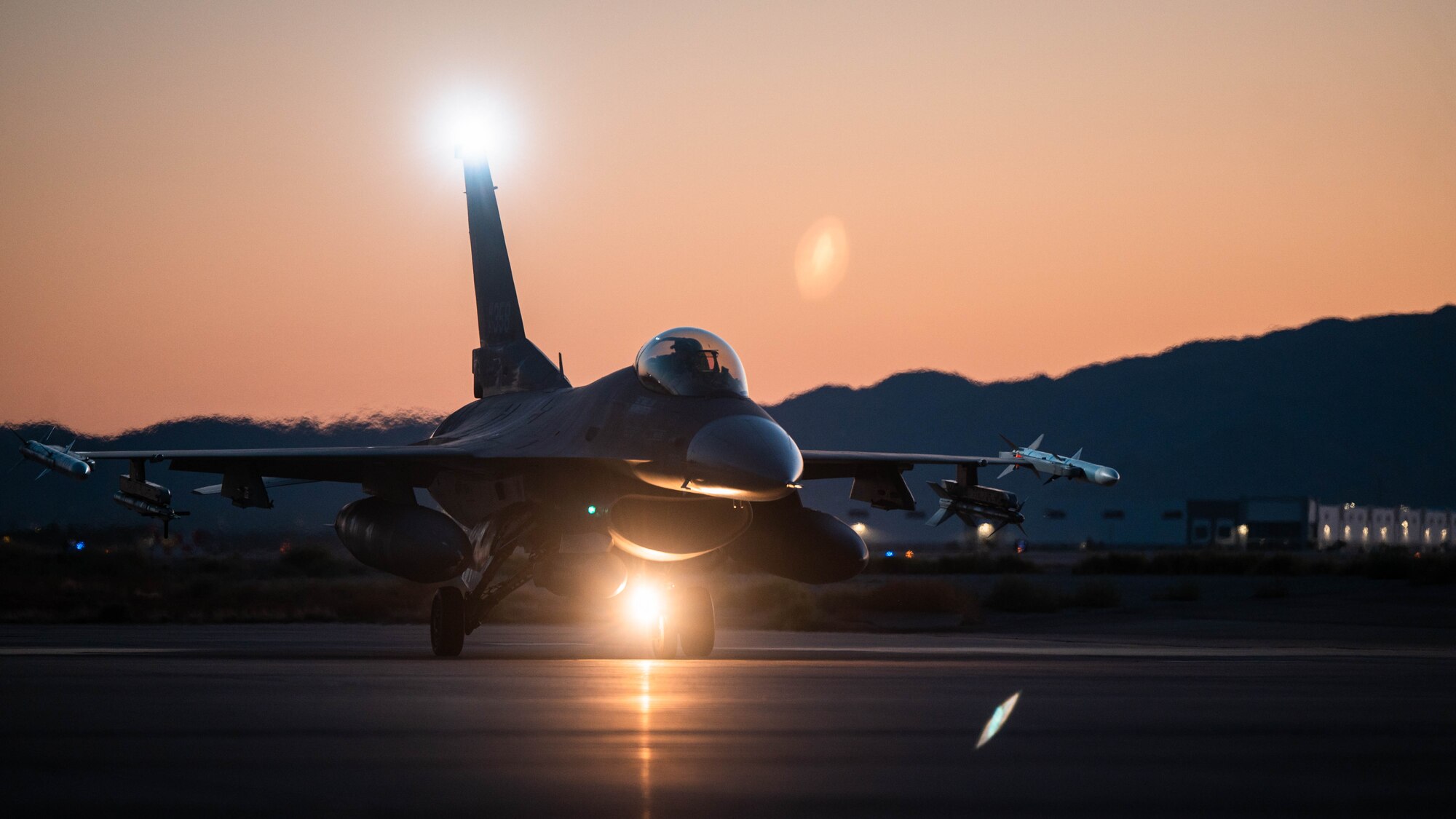 An F-16 Fighting Falcon sits idle on the Luke Air Force Base Flightline with a sunset behind it