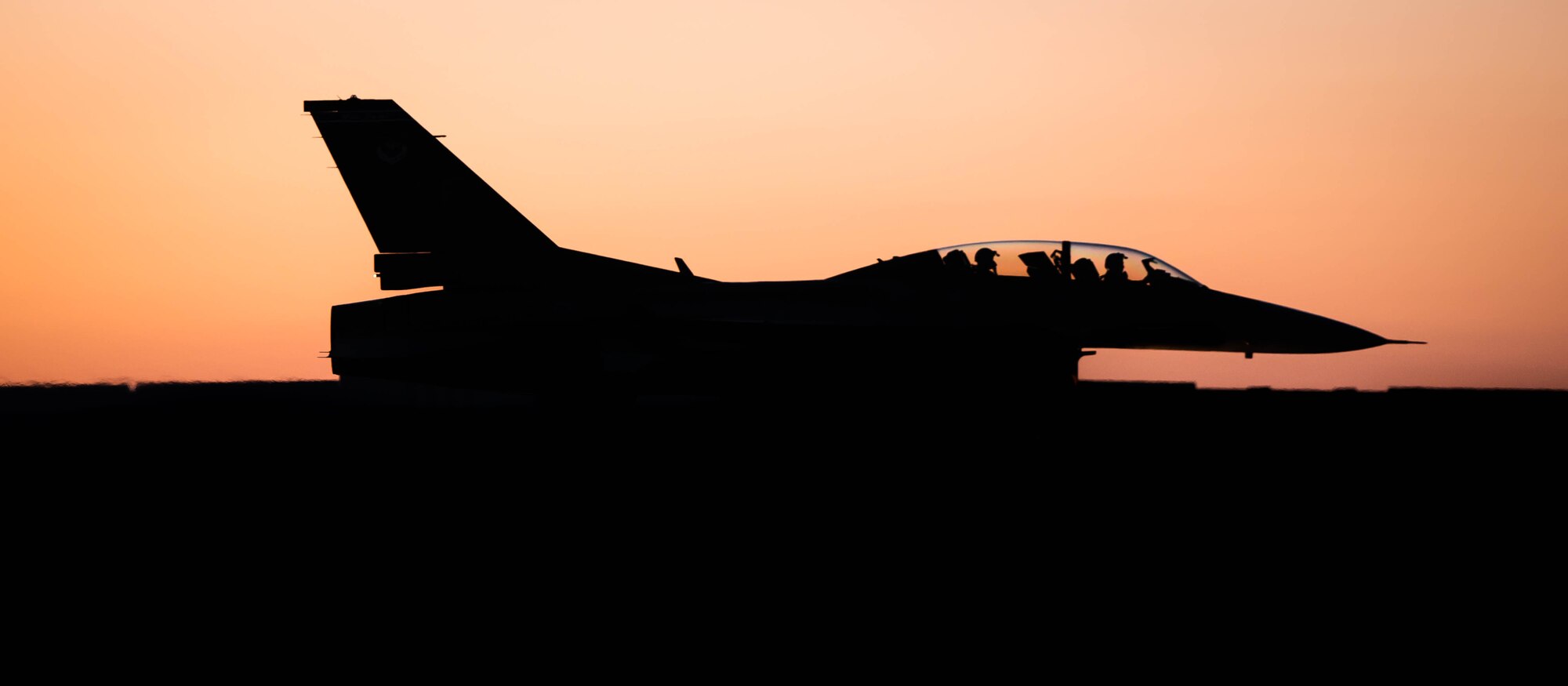 A silhouette of an F-16 Fighting Falcon sits idle on the Luke Air Force Base Flightline with a sunset behind it