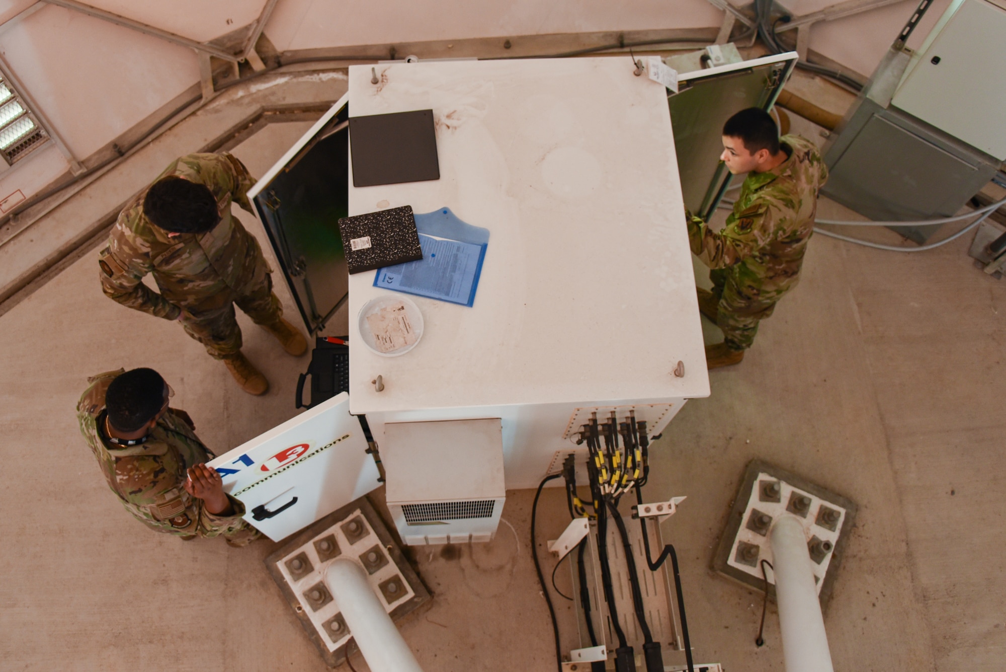 Three airmen in green uniforms look into a white cabinet.