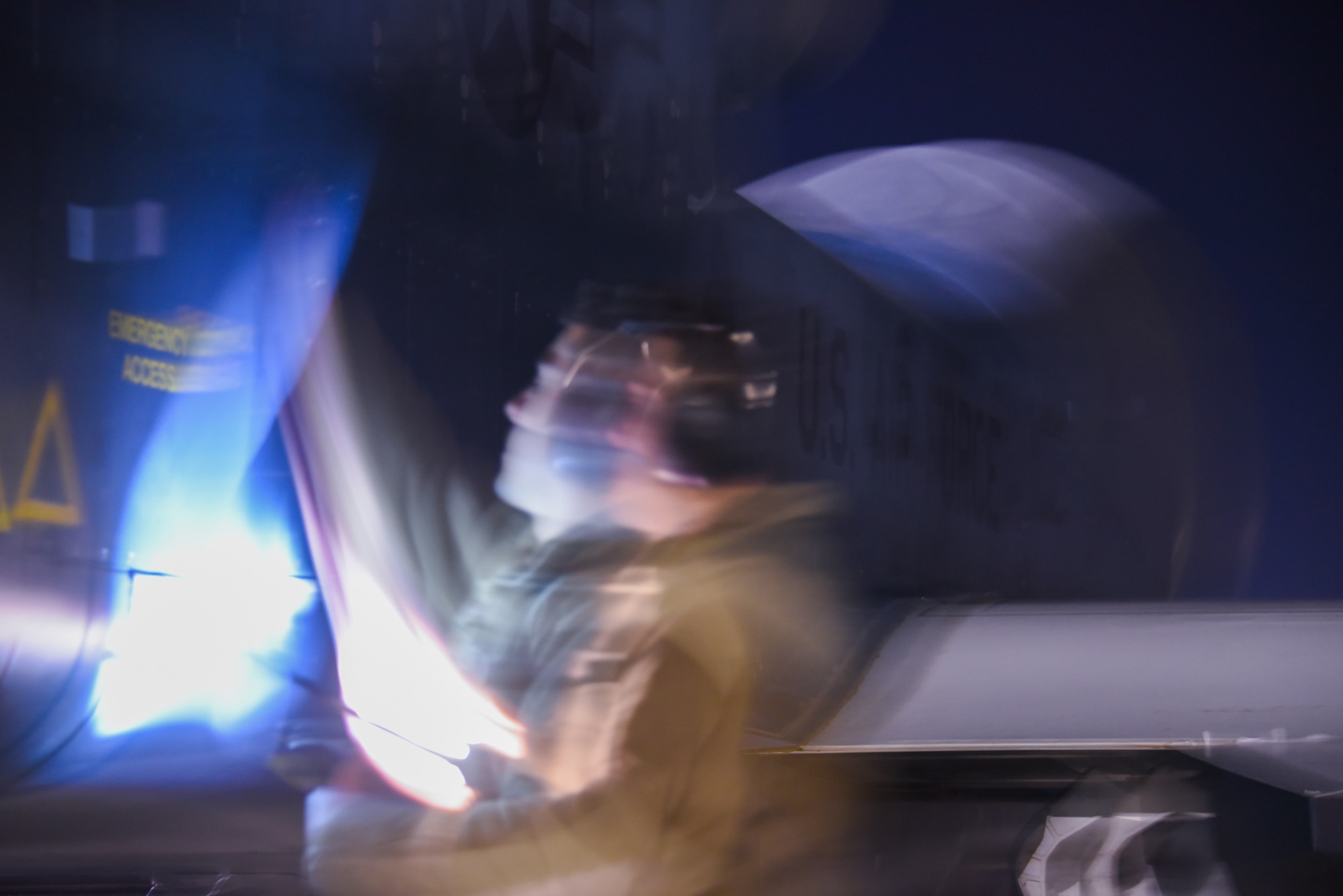 A burred image shows a male airman holding a flashlight and opening a panel of an RQ-4 Block 40.