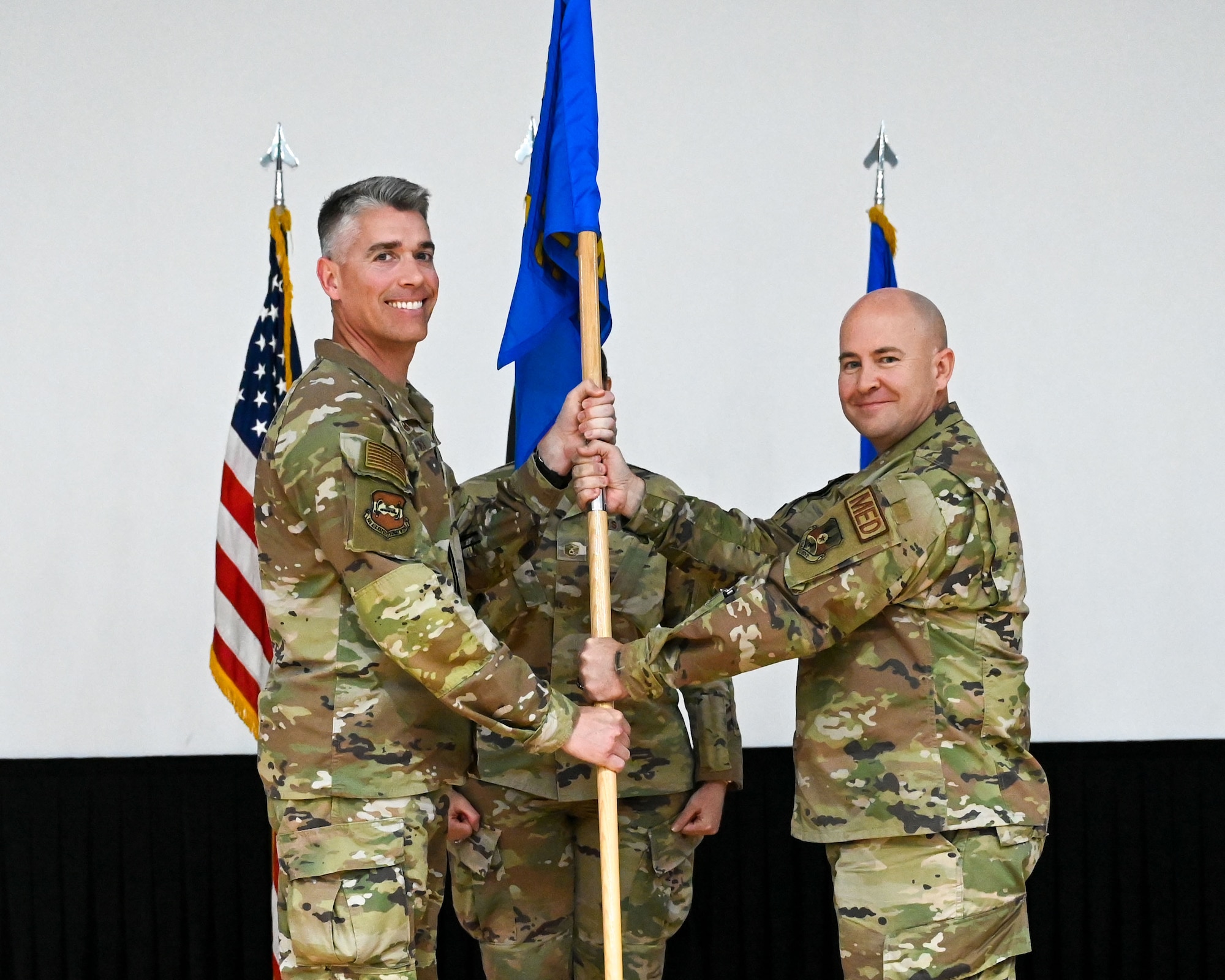 Col. George Buch, 386th Air Expeditionary Wing commander, passes the guidon to Lt. Col. Christopher Parker, incoming 386th EMDS commander, during a change of command ceremony at Ali Al Salem Air Base, Kuwait, May 30, 2023. The passing of the guidon symbolizes the passing of command from one commander to the next.