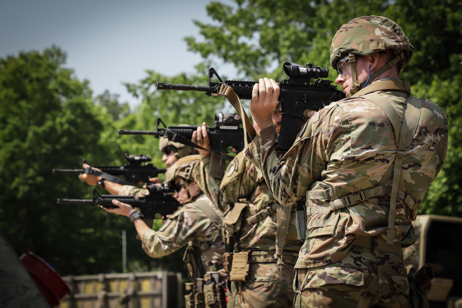 Multiple Soldiers in a line engage targets with a rifle.