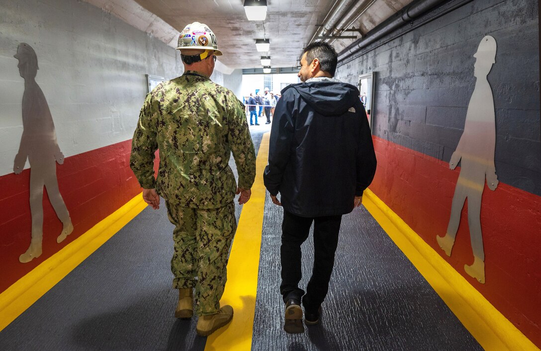 Capt. Jip Mosman, commander, Puget Sound Naval Shipyard & Intermediate Maintenance Facility, in Bremerton, Washington, tours the newly renovated Burwell Tunnel with Geno Hernandez, Sr. Visual Information Specialist, PSNS & IMF Public Affairs Office, following the ribbon-cutting ceremony May 9, 2023. Hernandez designed and illustrated the overall atheistic with added graphic embellishment created by his design partner Robin Lee, Visual Information specialist, PSNS & IMF Public Affairs Office. (U.S Navy photo by Wendy Hallmark)