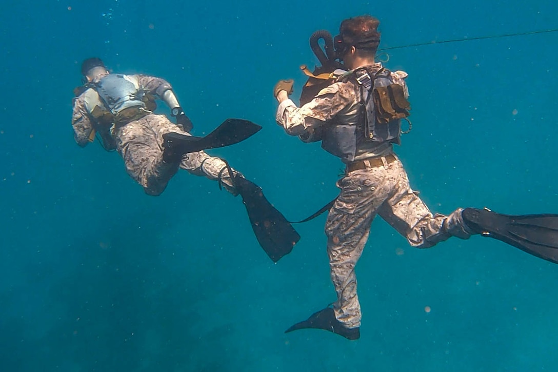 Marines, wearing their uniforms, swim in open water.