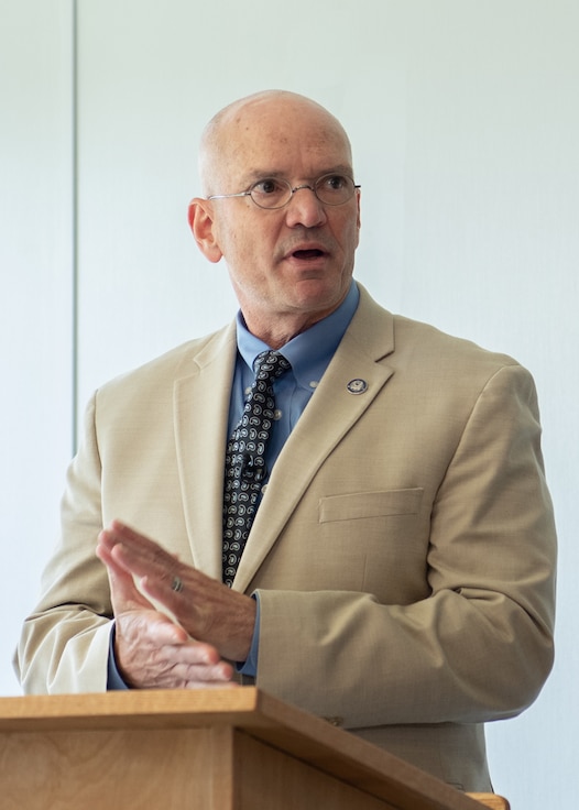 A man in a light suit speaks from behind a podium