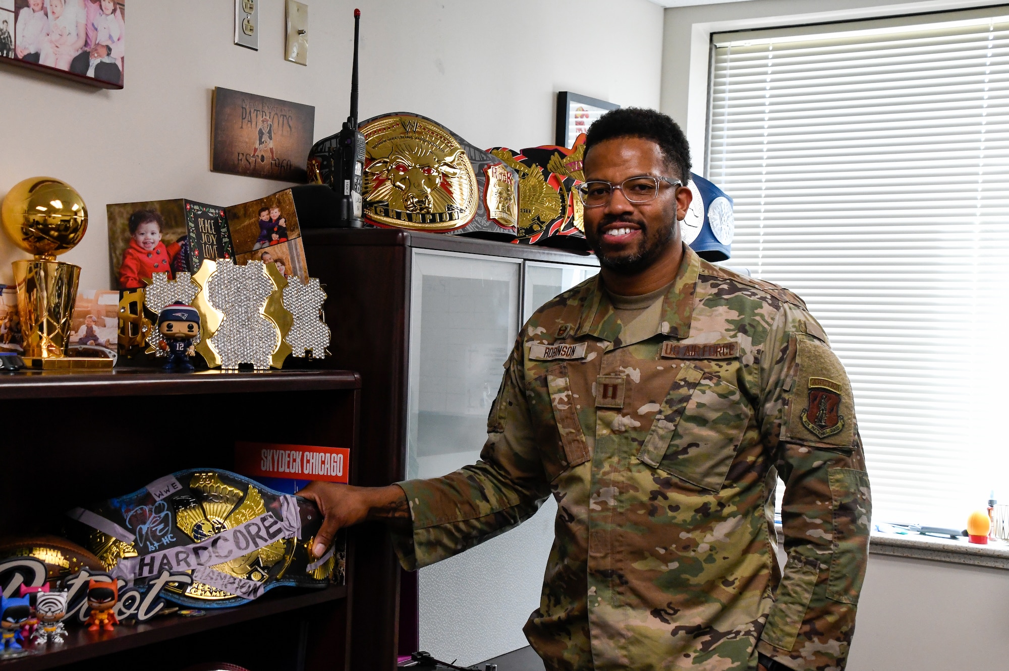 Capt. Anthony Robinson, 168th Communications Squadron commander, poses for a photo holding wrestling championship belts representing his wife, mother, and grandmother in his office. The wrestling belts are on display in his office, reminding him of his loved ones, his family’s inspiration, memories spent with his family, where he has come from, and his upbringing. (U.S. Air National Guard photo by Senior Master Sgt. Julie Avey)