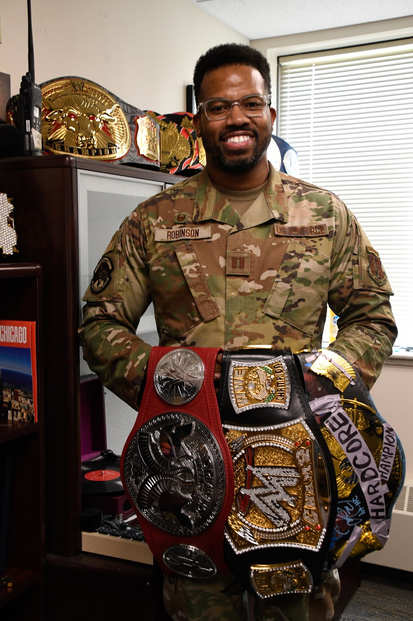 Capt. Anthony Robinson, 168th Communications Squadron commander, poses for a photo holding wrestling championship belts representing his wife, mother, and grandmother in his office. The wrestling belts are on display in his office, reminding him of his loved ones, his family’s inspiration, memories spent with his family, where he has come from, and his upbringing. (U.S. Air National Guard photo by Senior Master Sgt. Julie Avey)