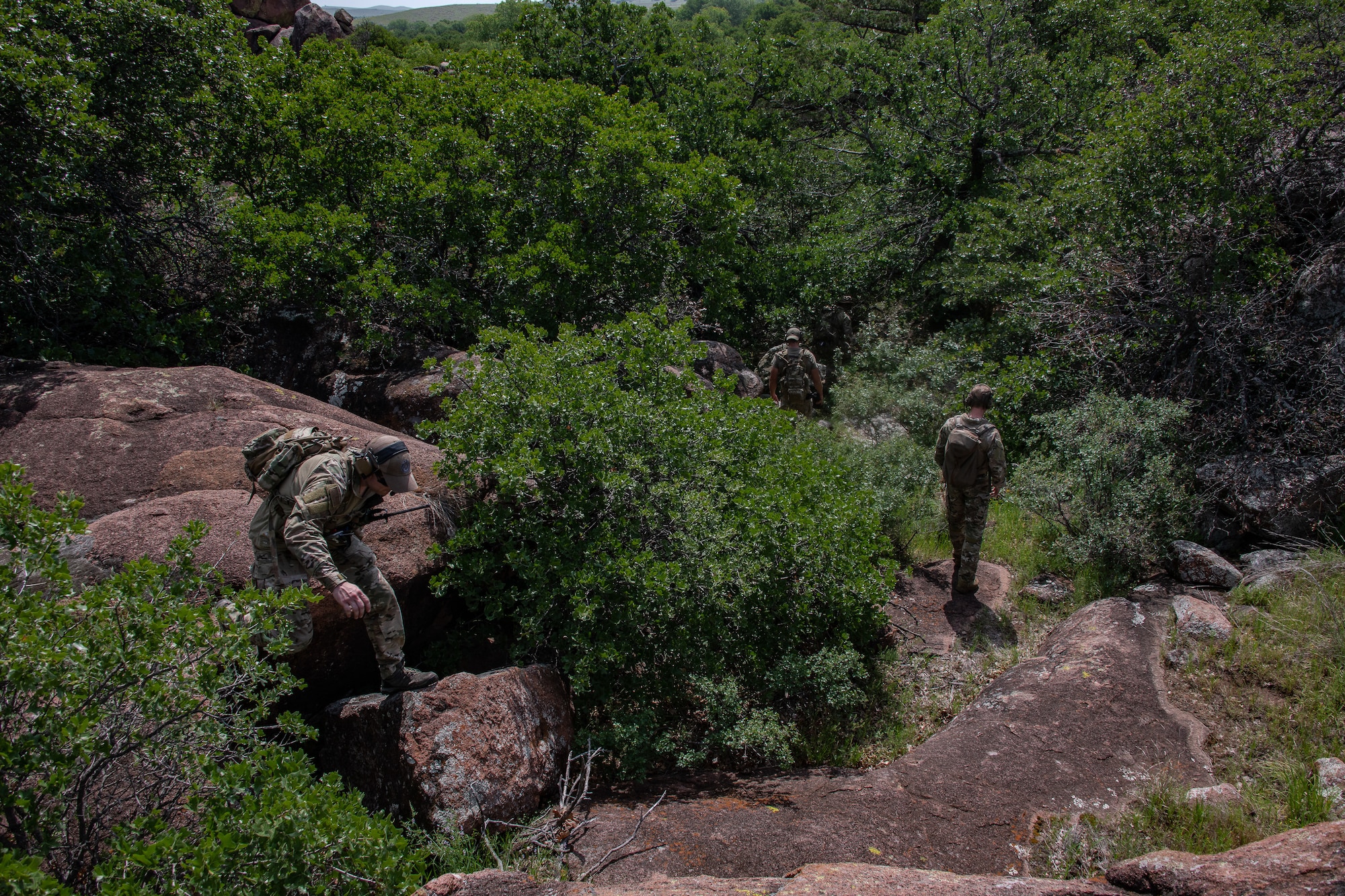 Airmen clamber over rocks and through trees