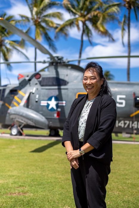 woman stands outdoors and smiles for a photo in front of a static display helicopter