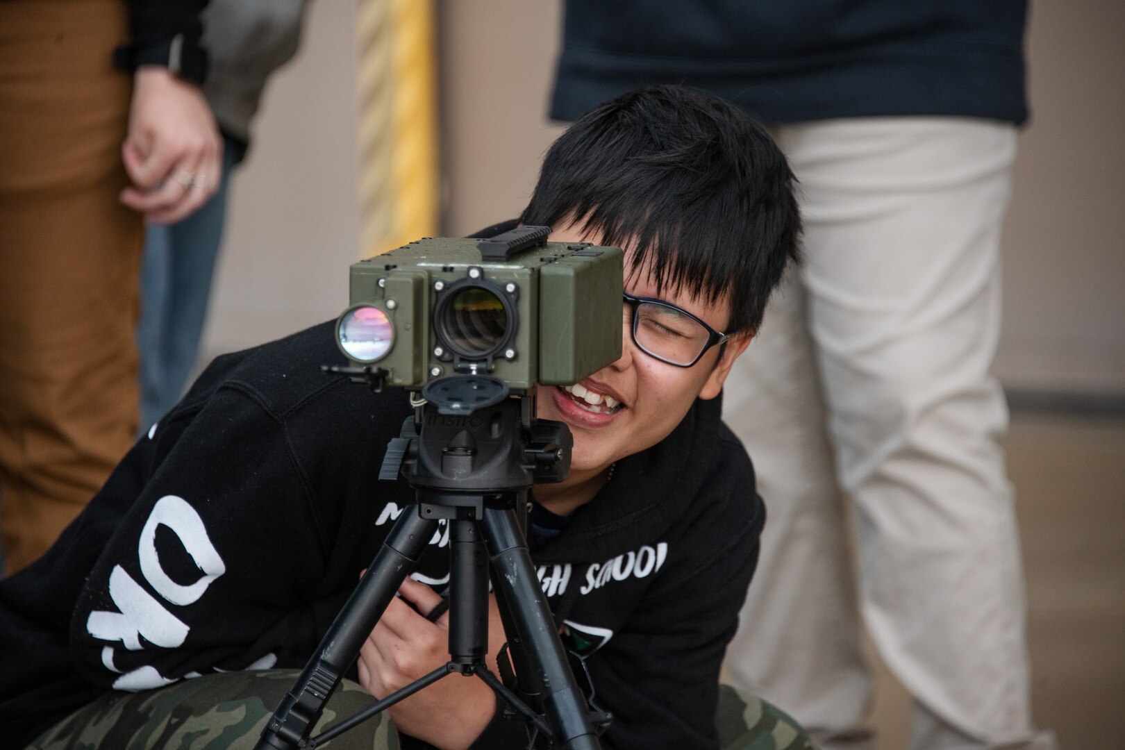 a high school students smiles as they stare through the viewfinder of a laser designator