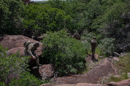 Airmen clamber over rocks and through trees