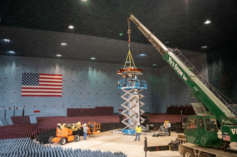 A construction crew works on an object in a large room.