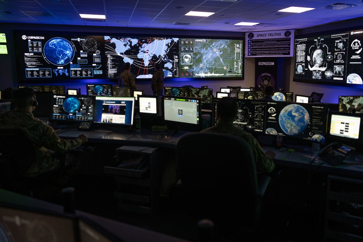 People sit in a room filled with monitors projecting maps and the Earth.