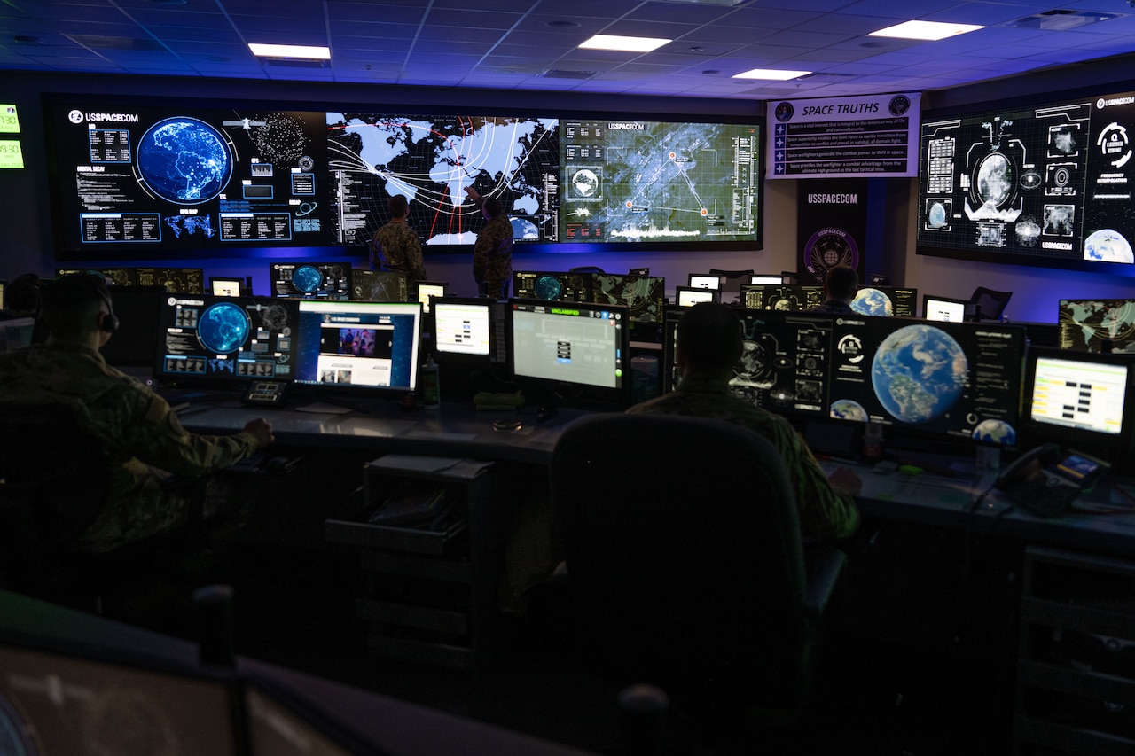 People sit in a room filled with monitors projecting maps and the Earth.