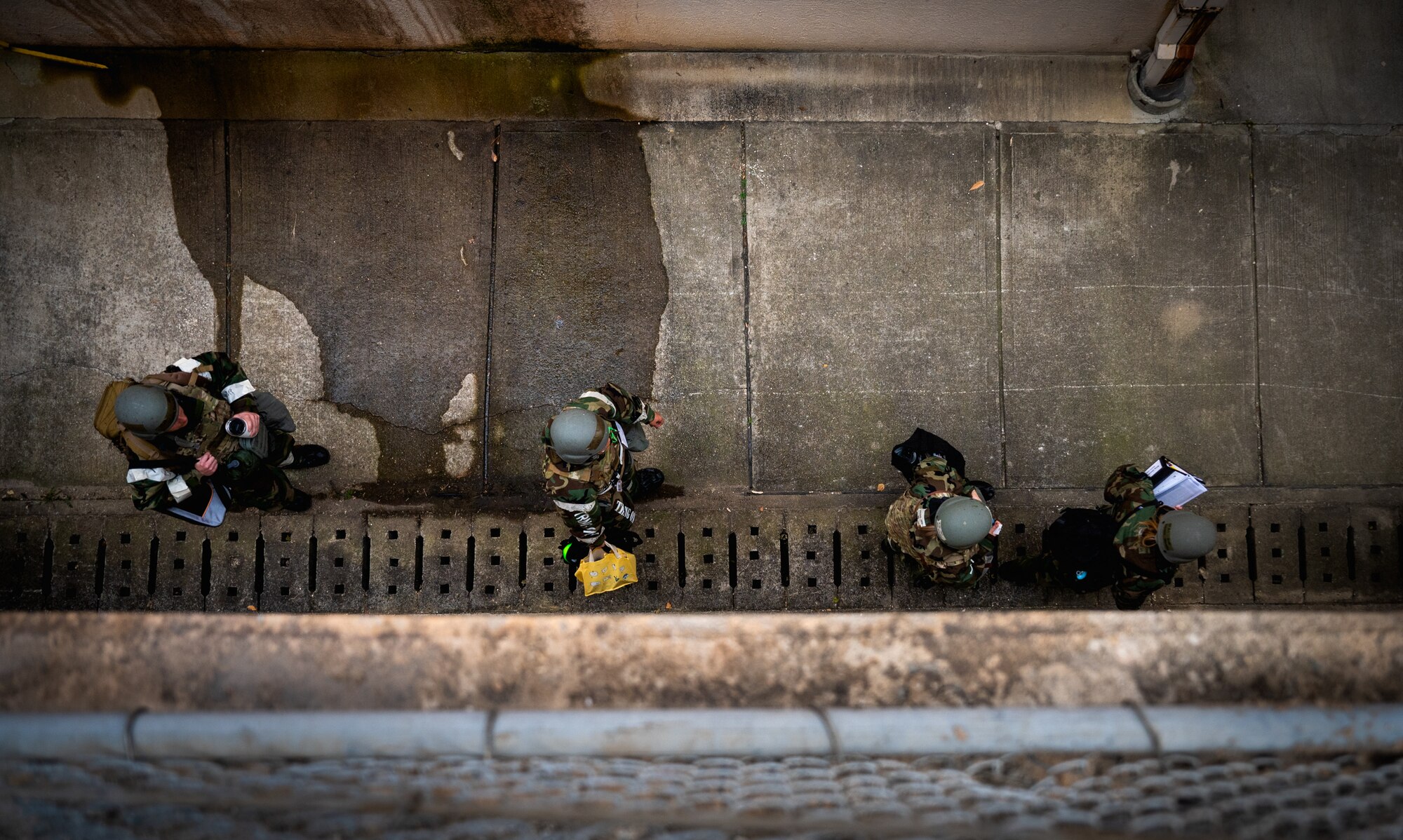 Four Airmen in MOPP gear walk through an alley.