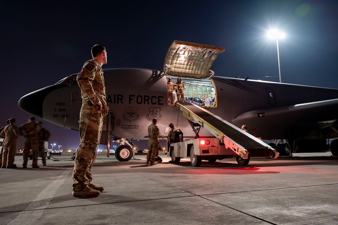 A senior officer watches as airmen prepare to unload cargo from a KC-135 Stratotanker.