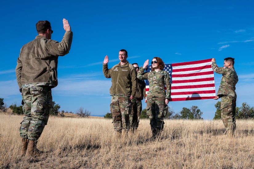 Two service members take the oath of enlistment in a field with an American flag behind them.