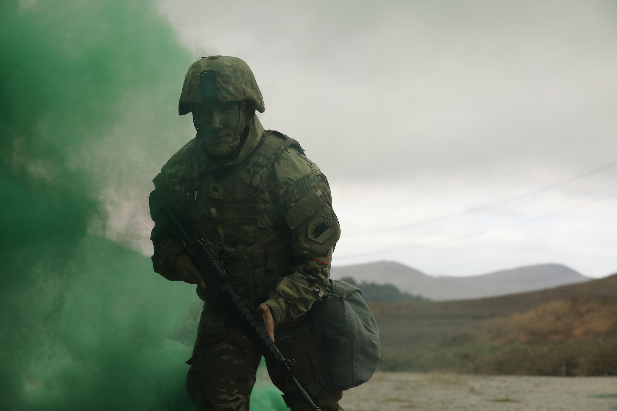 U.S. Army Sgt. Shayan Mirzazadeh, an intelligence analyst with Joint Forces Headquarters, California National Guard, runs through green smoke toward a simulated combat casualty event at Camp San Luis Obispo on Day 3 of the 2024 Best Warrior Competition, Oct. 25, 2023.