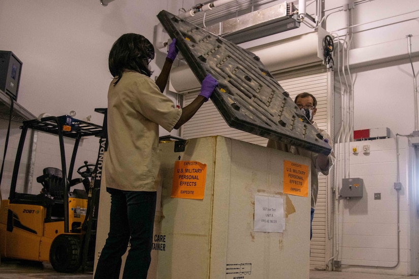 Two people open the lid to a large crate.