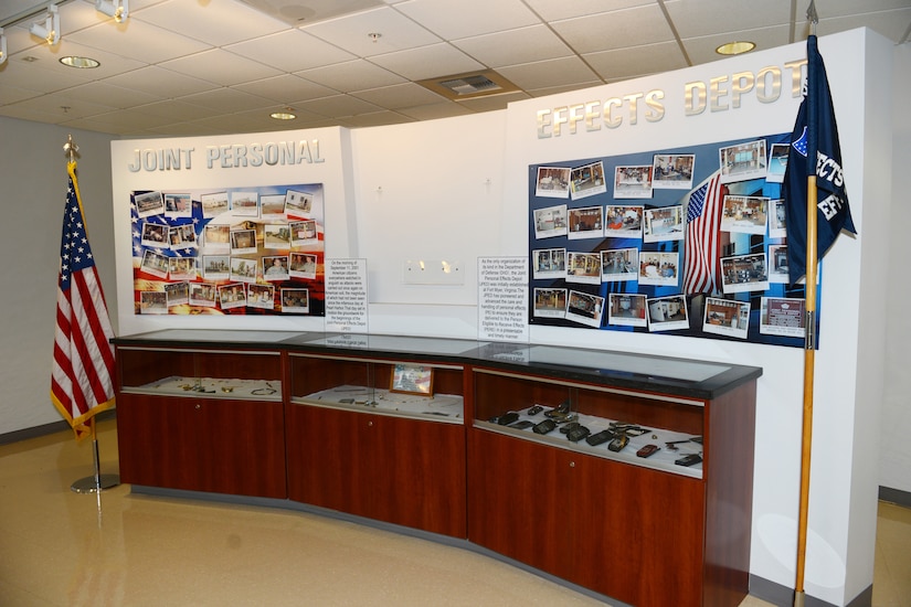 Three display cases sit below photos and a large sign that says Joint Personal Effects Depot. Flags are placed at opposite sides of the cases.