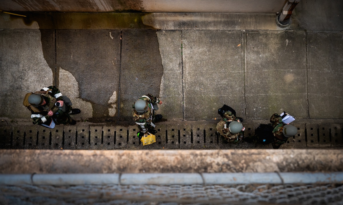 Four Airmen in MOPP gear walk through an alley.