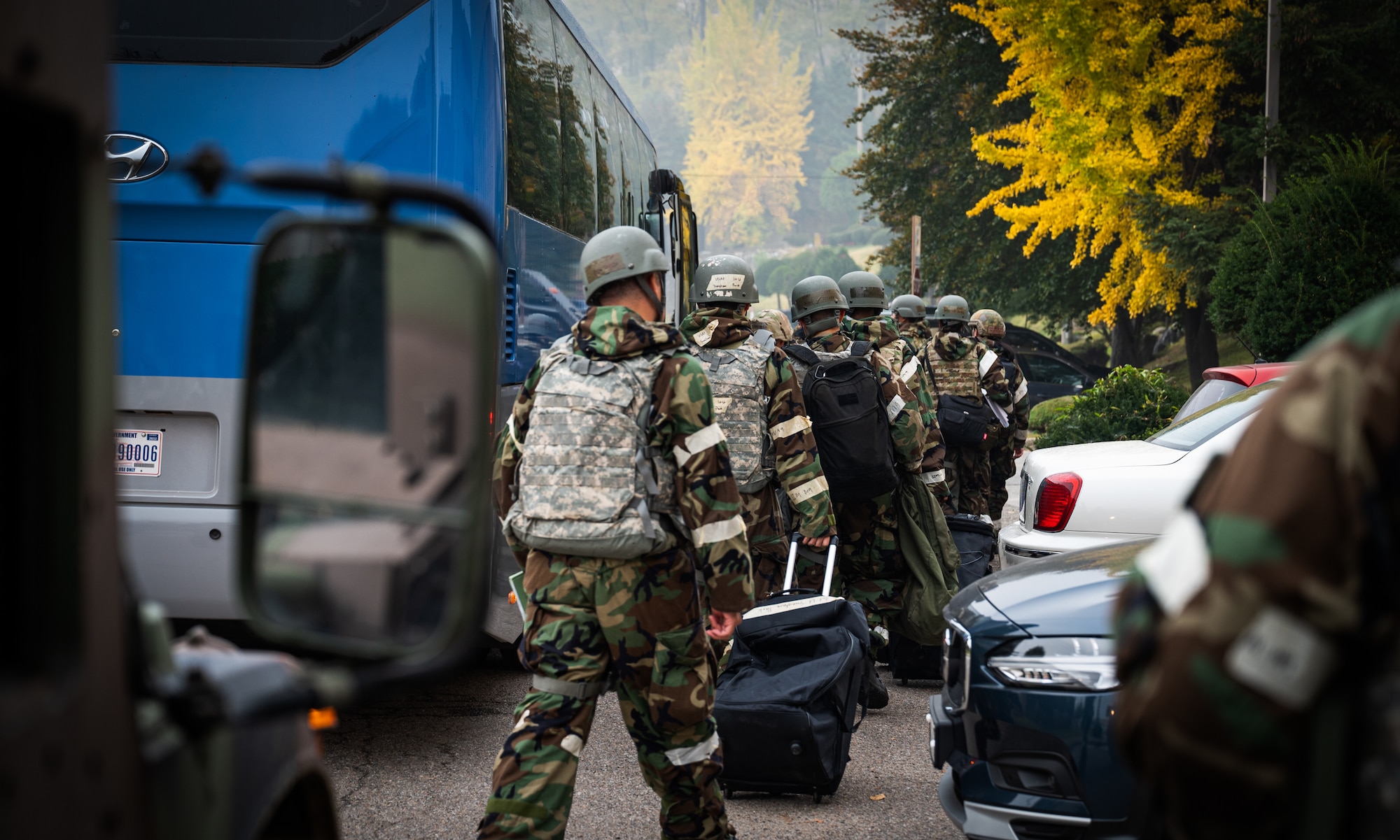 Airmen in MOPP gear load onto a bus.