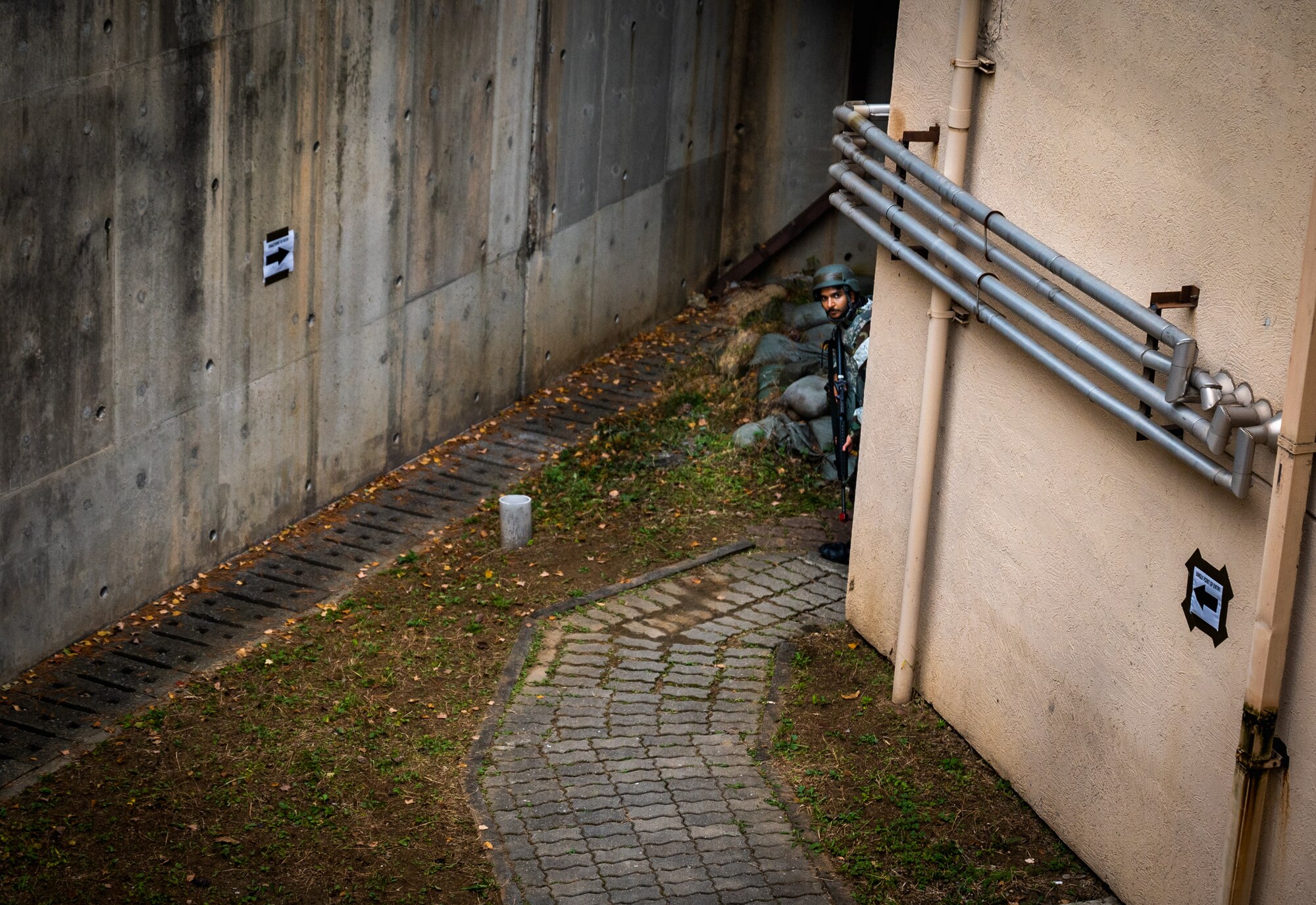 Four Airmen in MOPP gear are lead by an SMT through an alley.