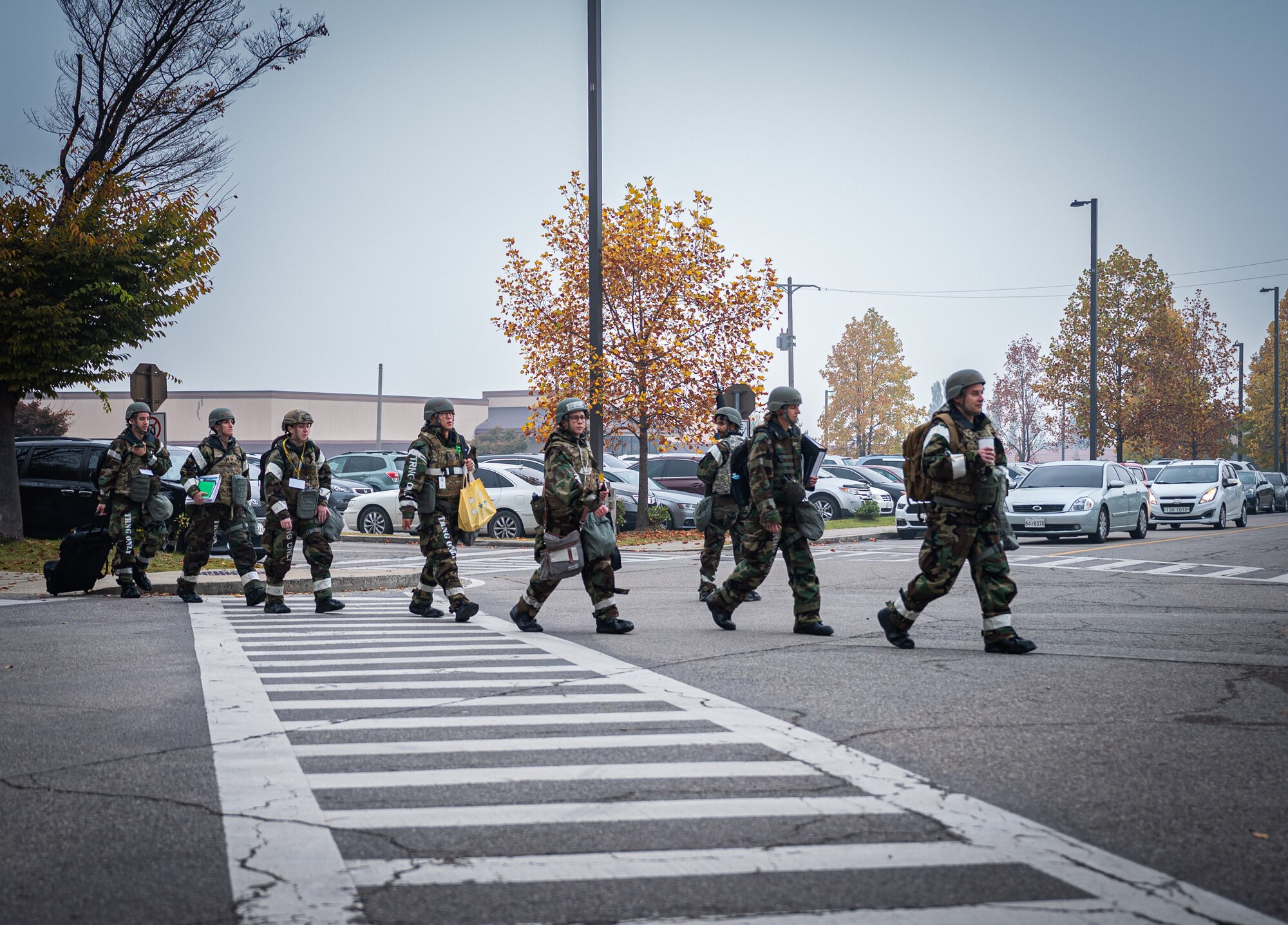Airmen in MOPP gear cross across a street.