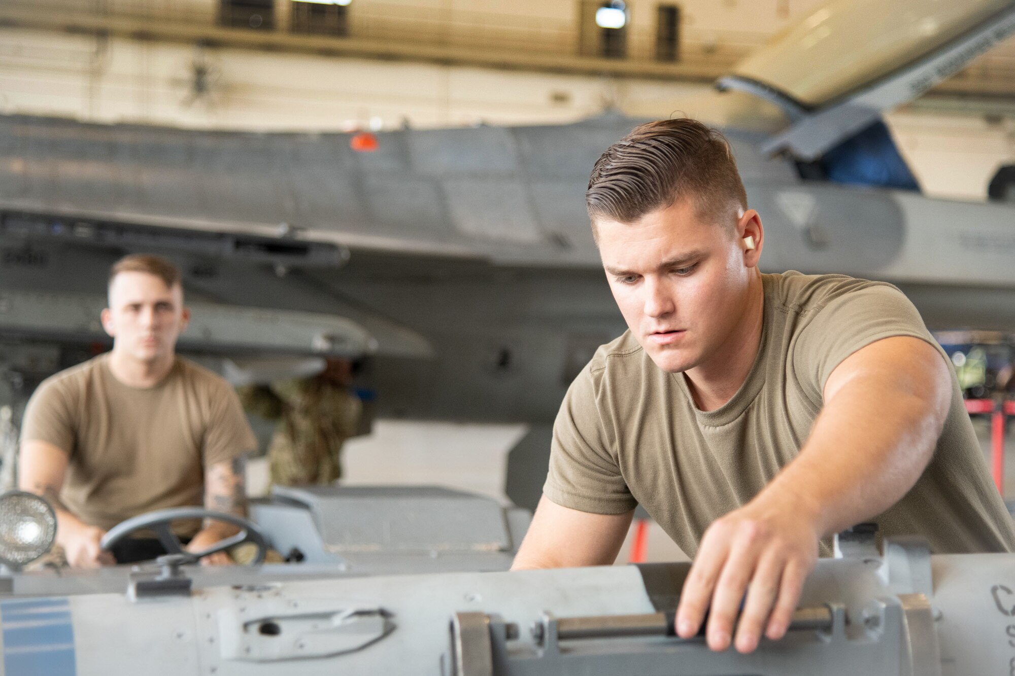 Airmen load a weapon to a vehicle, an F-16 Fighting Falcon behind them.