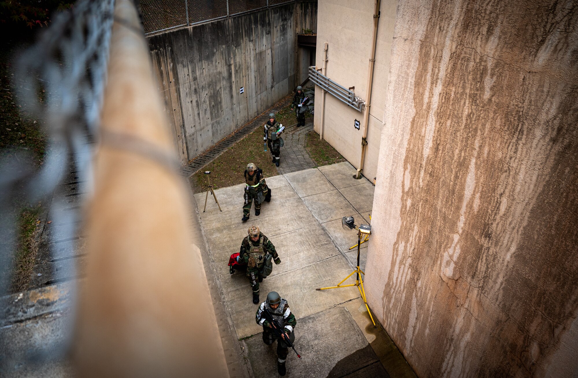 Four Airmen in MOPP gear are lead by an SMT through an alley.