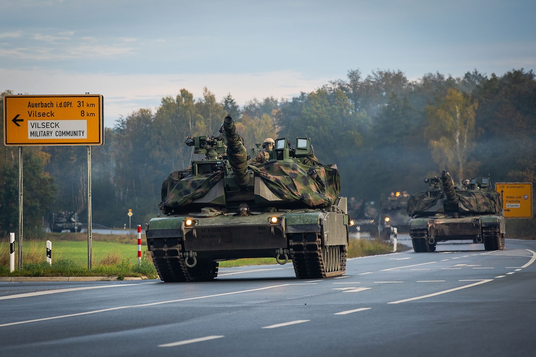 Tanks drive down a street in a tactical road march.