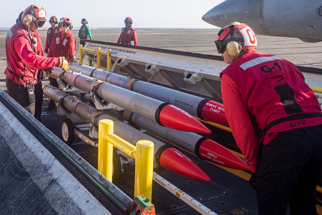 Sailors move ordnance on a flight deck at sea.