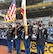 Four Soldiers in uniform stand on the field of a baseball stadium. A male and female Soldier hold flags, while the other male and female Soldiers hold guns.
