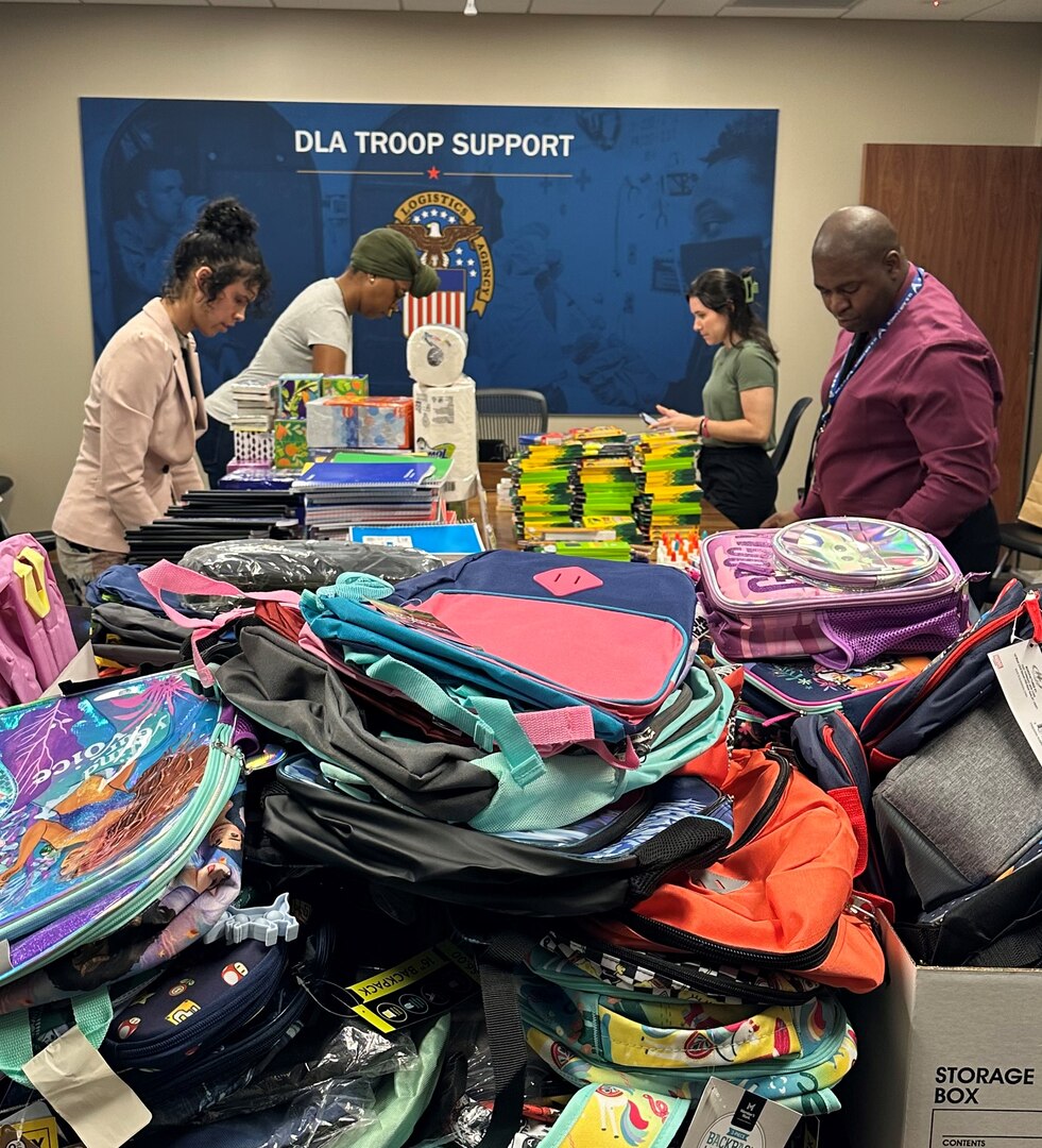 men and women standing around table with backpacks and school supplies