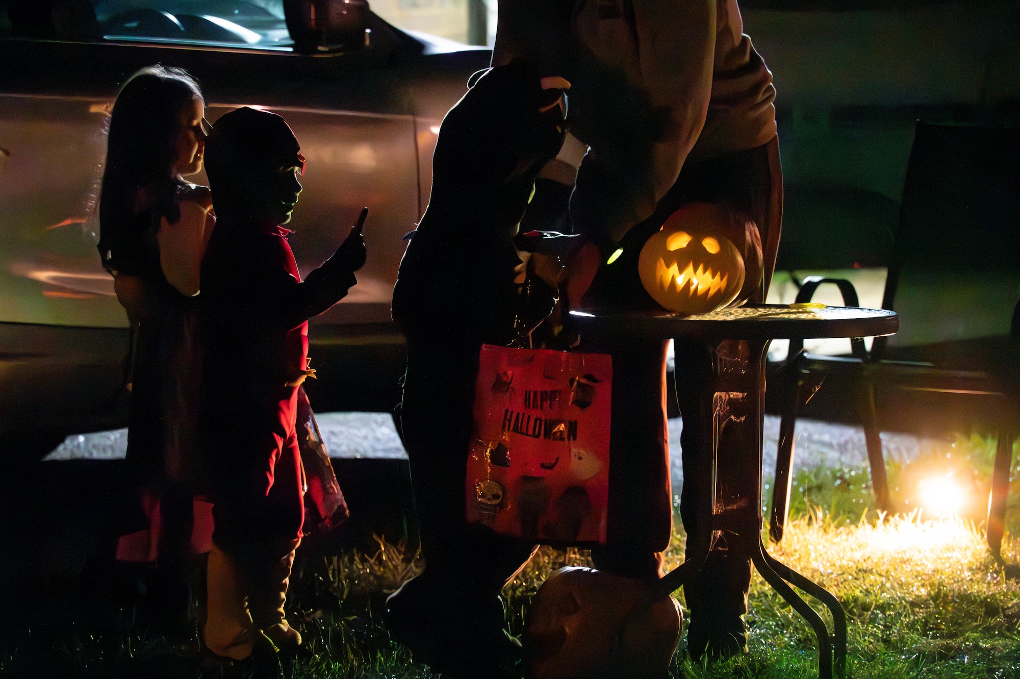The silhouettes of local children approach a jack-o-lantern